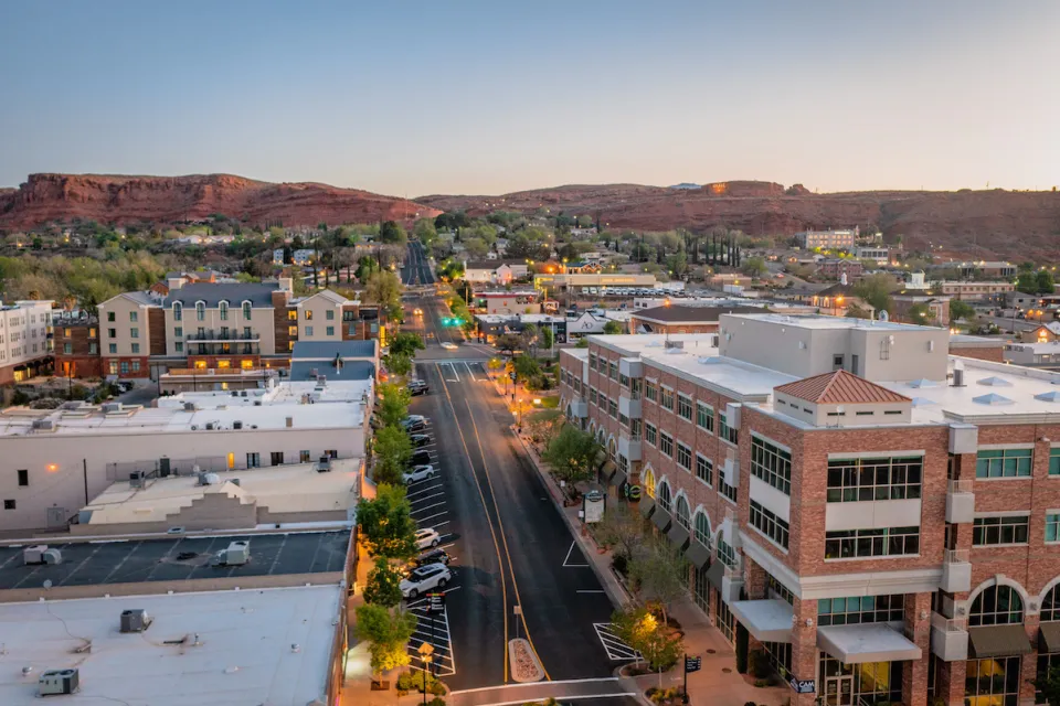 Aerial view of wide street in St. George, Utah at dusk with red rock mountains in background.